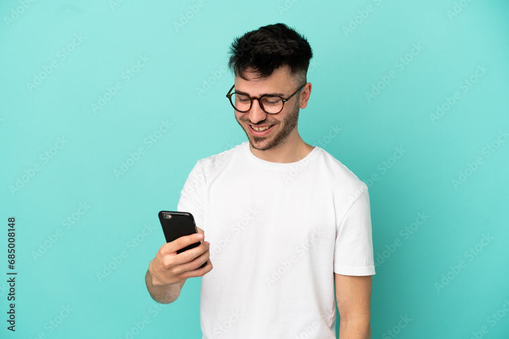 Young caucasian man isolated on blue background sending a message or email with the mobile Young caucasian man isolated on blue background sending a message or email with the mobile
