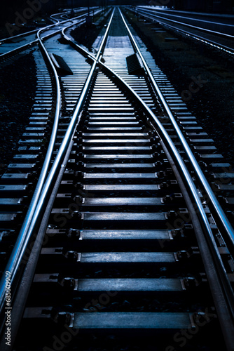 Fototapeta Naklejka Na Ścianę i Meble -  Railway switch of a railroad side track in Germany. Blue hour twilight reflecting on wooden thresholds an glistening steel rails in evening atmosphere. Symbol for decisions an safety in transportation