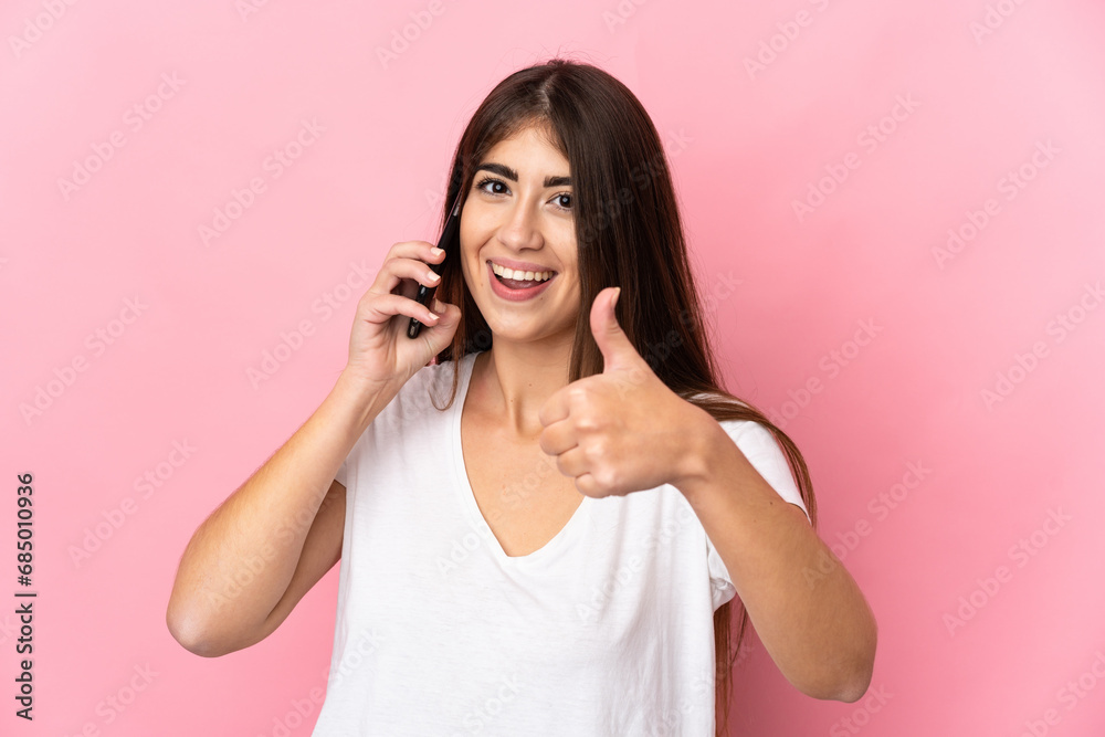Young caucasian woman isolated on pink background keeping a conversation with the mobile while doing thumbs up Young caucasian woman isolated on pink background keeping a conversation with the mobile while doing thumbs up