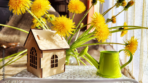 miniature toy house in dandelion flowers and watering can. natural background. symbol of family and rural, rustic life. mortgage, construction, rental, property concept. Eco Friendly home. copy space © keleny