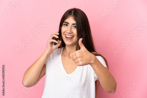 Young caucasian woman isolated on pink background keeping a conversation with the mobile while doing thumbs up