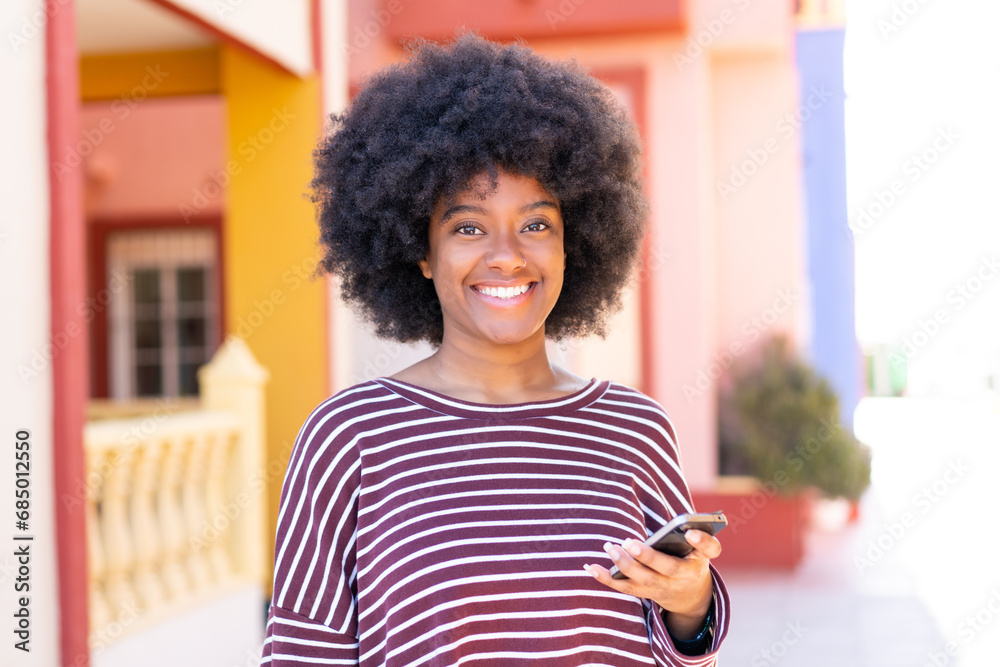 Fototapeta premium African American girl using mobile phone at outdoors smiling a lot