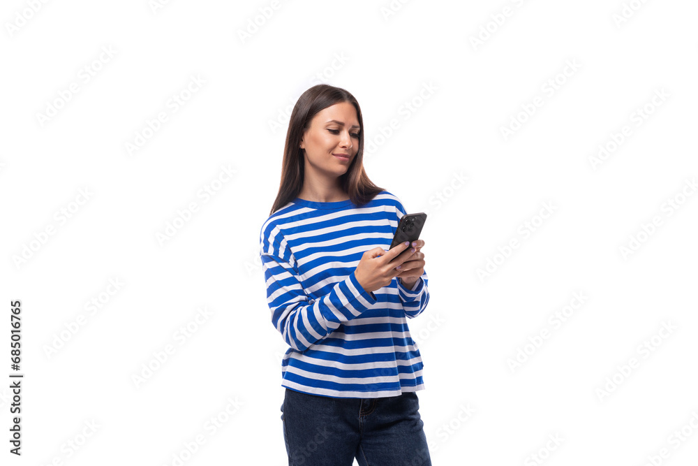 young charming brunette lady with straight hair dressed in a blue sweater uses a phone for social networks
