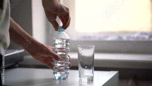 person holds a bottle and pour water in the glass