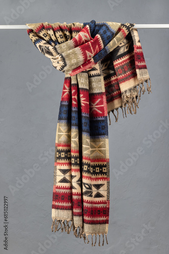 Cashmere scarf with fringe hanging on a hanger. Home comfort. Colorful plaids on a gray background.