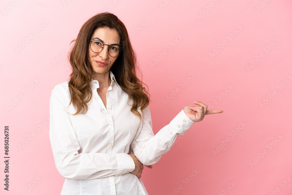 Middle aged caucasian woman isolated on pink background pointing finger to the side - obrazy, fototapety, plakaty 