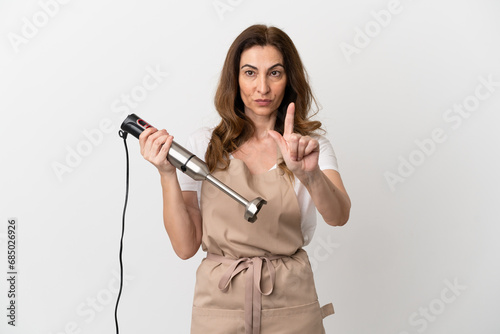 Middle aged caucasian woman using hand blender isolated on white background showing and lifting a finger