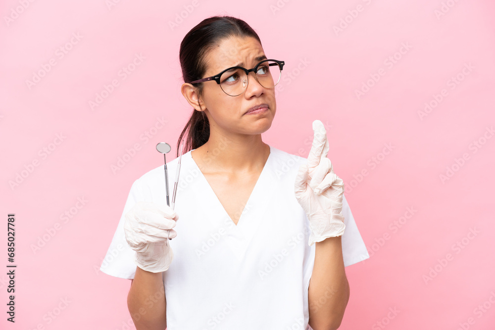 Dentist Colombian woman isolated on pink background with fingers crossing and wishing the best Dentist Colombian woman isolated on pink background with fingers crossing and wishing the best