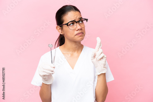 Dentist Colombian woman isolated on pink background with fingers crossing and wishing the best