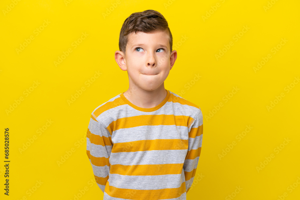 Little caucasian boy isolated on yellow background having doubts while looking up - obrazy, fototapety, plakaty 