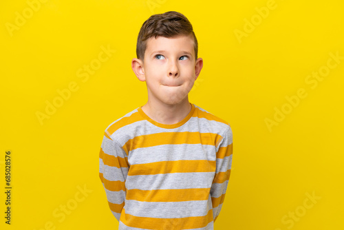 Little caucasian boy isolated on yellow background having doubts while looking up photo