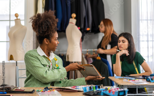 Portrait of young african american woman and young girl fashion designer stylish sitting and working with color samples.Attractive team designer girl work with colorful fabrics at fashion studio