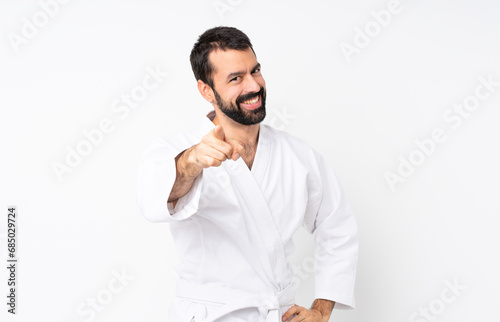 Young man doing karate over isolated white background points finger at you with a confident expression