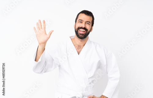 Young man doing karate over isolated white background saluting with hand with happy expression © luismolinero
