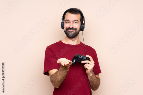 Man playing with a video game controller over isolated wall holding copyspace imaginary on the palm to insert an ad