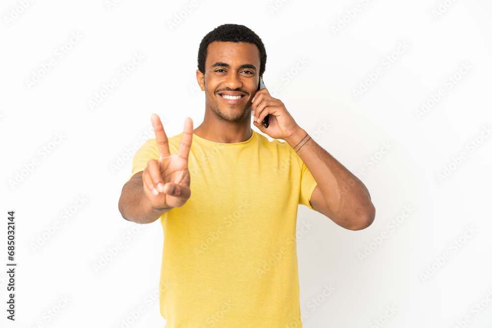 African American handsome man using mobile phone over isolated white background smiling and showing victory sign African American handsome man using mobile phone over isolated white background smiling and showing victory sign