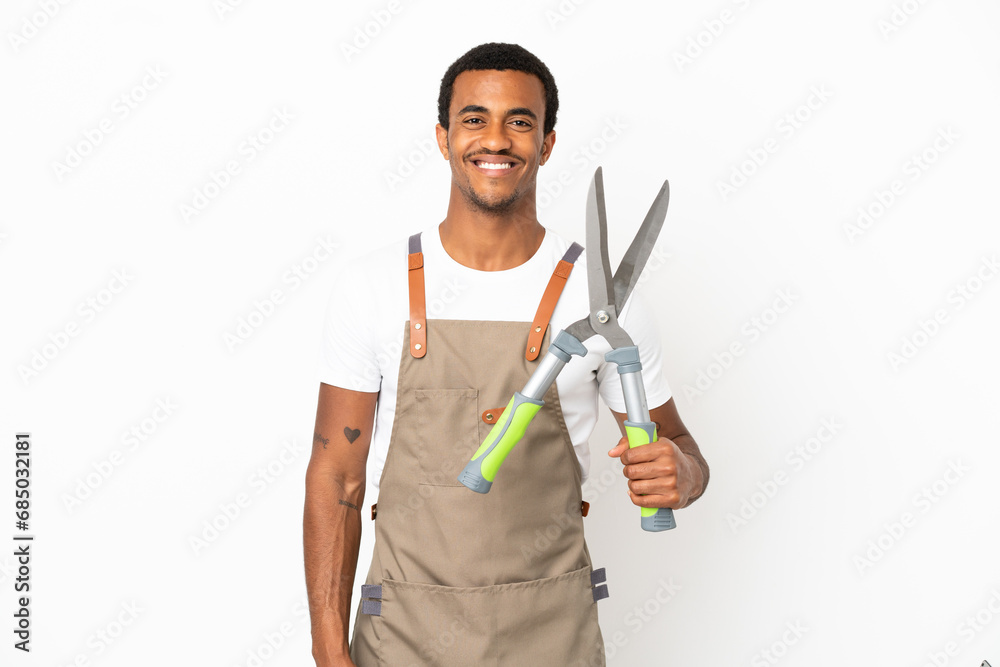 African American gardener man holding pruning shears over isolated white background posing with arms at hip and smiling African American gardener man holding pruning shears over isolated white background posing with arms at hip and smiling