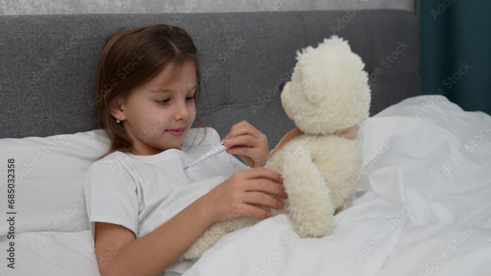 Cute child girl measure temperature of teddy bear toy Cute child girl measure temperature of teddy bear toy