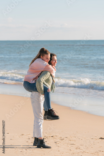 Happy female friends enjoying piggyback ride on beach