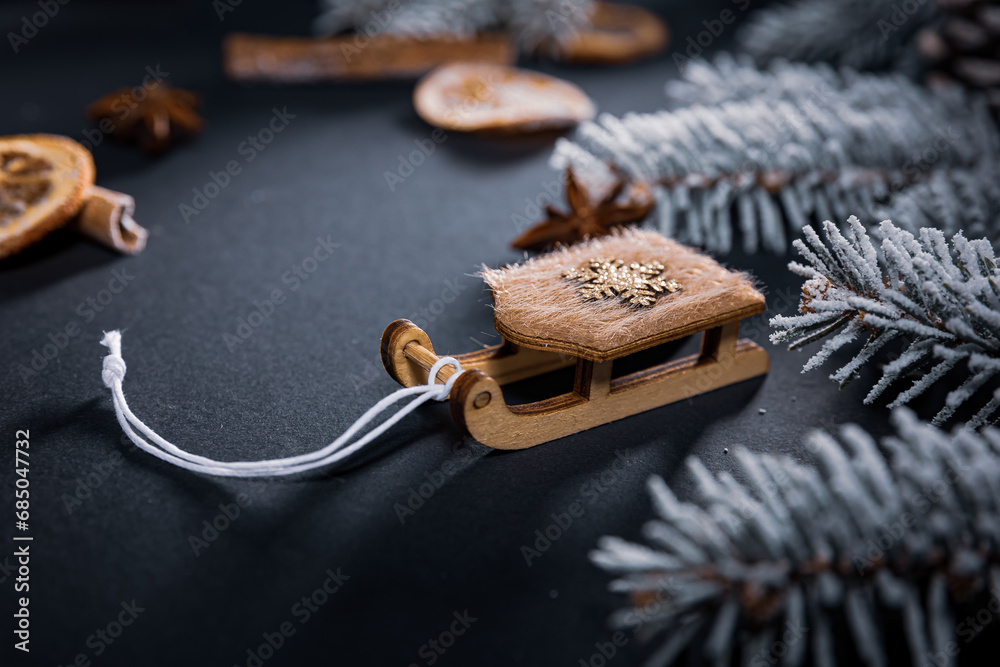 Fototapeta premium A sleigh with a star on a dark table among dried pieces of orange and cinnamon and branches of a Christmas tree covered with snow