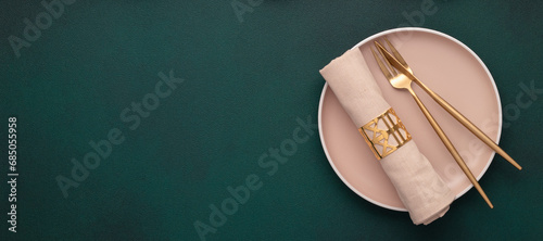 Plate with fork and knife. Mockup with empty space. Gold cutlery, dark green background. Top view. Celebration place setting, fabric napkin. Dining table in restaurant. Menu template, flat lay, banner