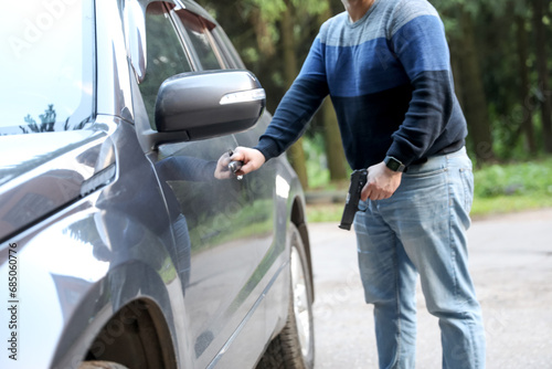 Defocused image. A man with a pistol in the parking lot opens the car. Crime, robbery.