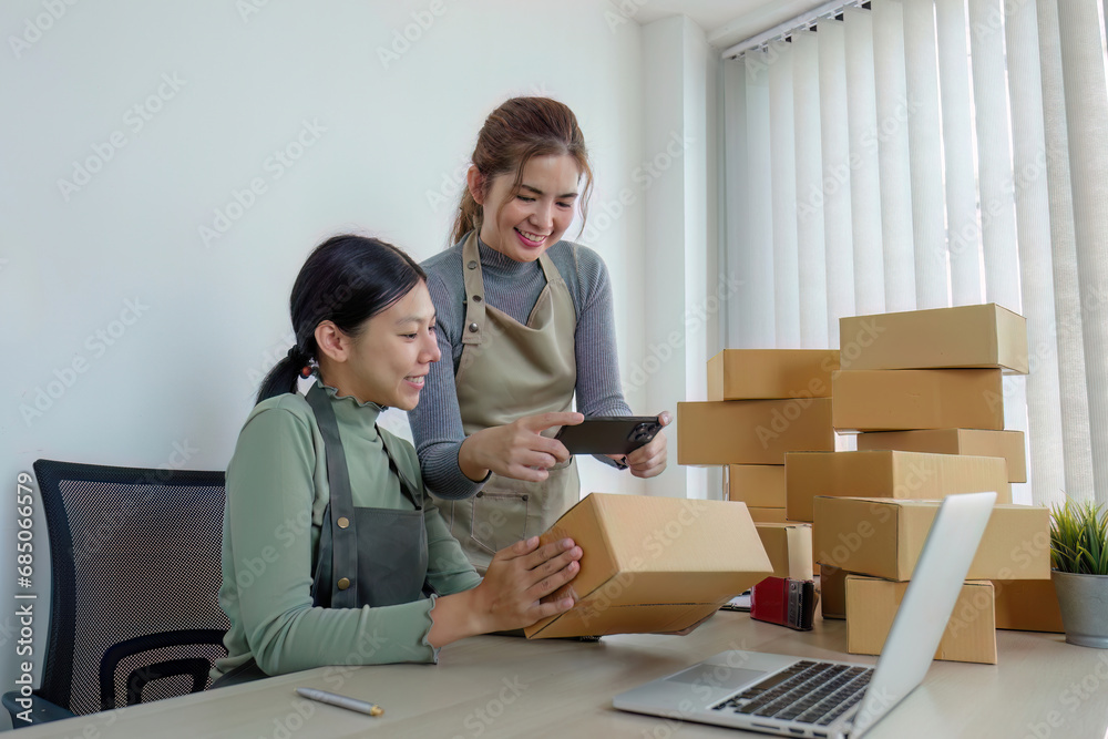 Two Asian entrepreneur women take order and check boxes of products according to customer orders in preparation for delivery. Two Asian entrepreneur women take order and check boxes of products according to customer orders in preparation for delivery.