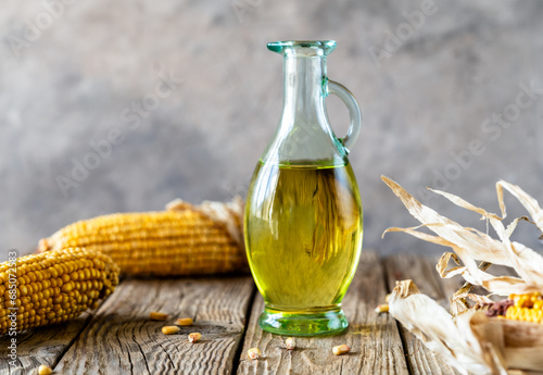 Corn oil in an oil jug with maize cobs over rustic wooden table and grey background