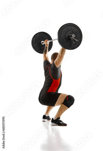 Side view. Muscular, athletic man, weightlifter training, lifting heavy barbell against white background