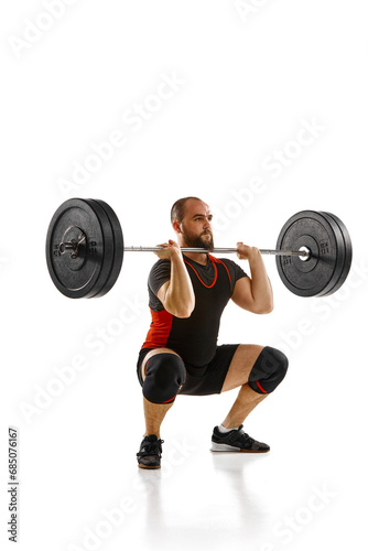 Focused bearded man, athlete with strong body training, lifting heavy weights, barbell against white background