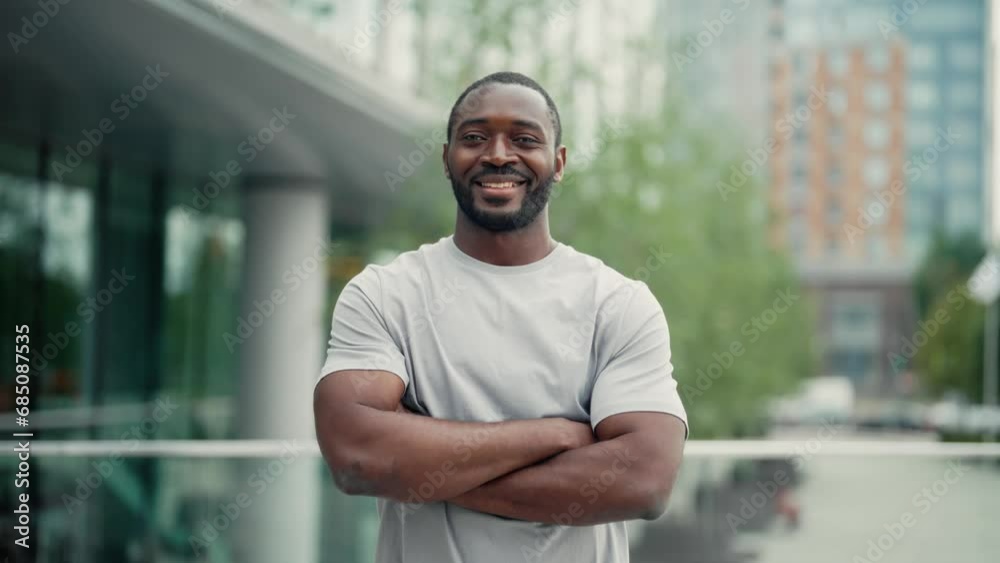 Portrait smiling positive african american bearded man standing on ctiy street in closed pose with hands on chest looking at camera. Friendly guy in t-shirt in downtown. Human emotions, body language. Portrait smiling positive african american bearded man standing on ctiy street in closed pose with hands on chest looking at camera. Friendly guy in t-shirt in downtown. Human emotions, body language.