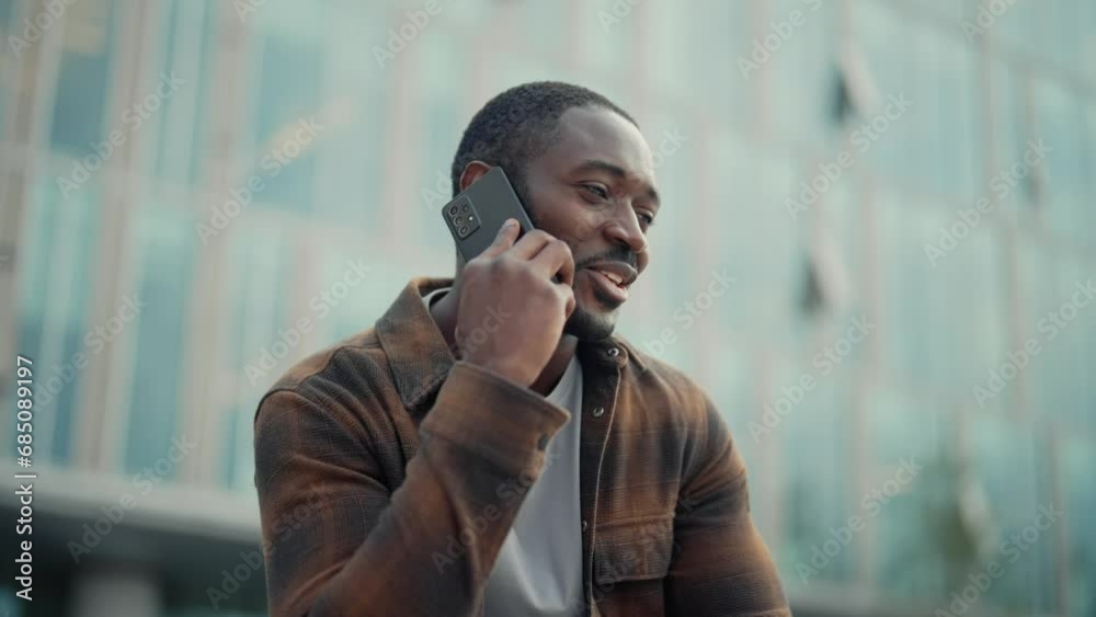 Portrait positive african american guy talking on smartphone gesturing hands sitting on street outdoors in city near modern building. Smiling guy calling phone having nice conversation explain things. Portrait positive african american guy talking on smartphone gesturing hands sitting on street outdoors in city near modern building. Smiling guy calling phone having nice conversation explain things.