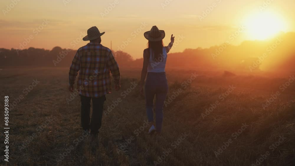 Farmer worker man manager in cap with tablet working on field talking with woman agronomist walking on harvesting ripe wheat at sunset. Food production, farmland, farm industry, agribusiness concept. Farmer worker man manager in cap with tablet working on field talking with woman agronomist walking on harvesting ripe wheat at sunset. Food production, farmland, farm industry, agribusiness concept.