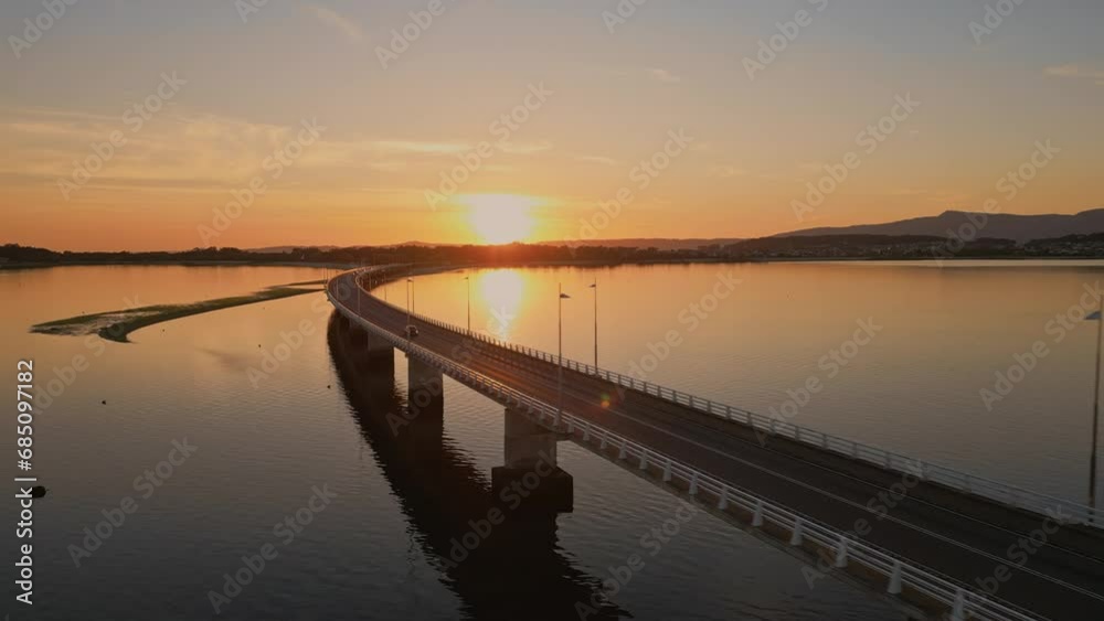 Establishing aerial view of a cars driving on a long sea bridge at sunset with a beautiful golden color reflect of the sea. Concept of transportation and travel in Spain Arosa Island Bridge Establishing aerial view of a cars driving on a long sea bridge at sunset with a beautiful golden color reflect of the sea. Concept of transportation and travel in Spain Arosa Island Bridge