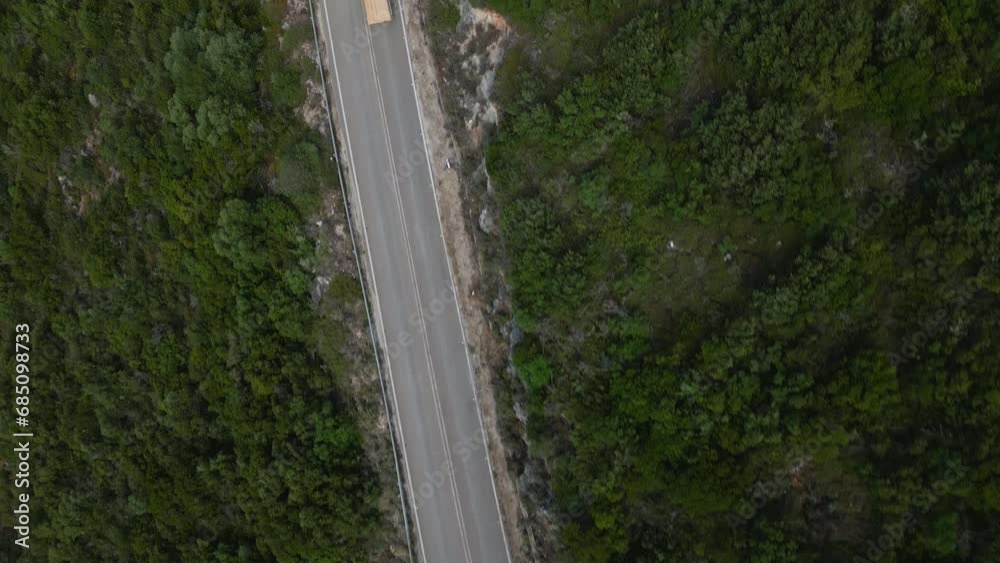 Aerial shot of a drone flying over a twisty mountain road by day. A truck with an open load bed drives on the road. Aerial shot of a drone flying over a twisty mountain road by day. A truck with an open load bed drives on the road.