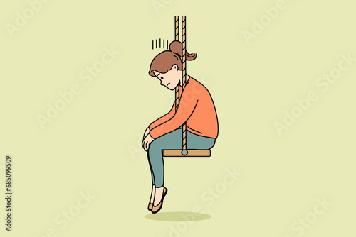 Upset little girl sits on swing with head down after parents divorce or reprimand at school. Upset schoolgirl is sad because of problems with friends who do not want to go out together