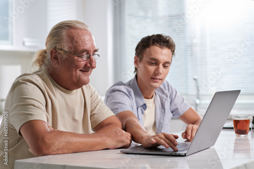 Young man showing elderly grandfather how to use various applications on laptop