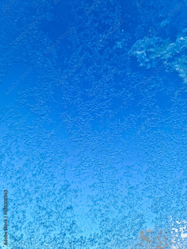 Frozen ice on a window with a blue sky background.