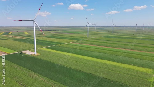 Aerial view of wind turbines in agricultural field. Drone footage of beautiful summer landscape with wind farm and clouds in the blue sky. Energy production with clean and renewable energy