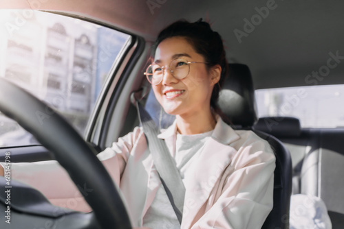 Front view of asian Thai woman wear eye glasses, happy smiling while driving a car alone on road, going to work in the morning. photo