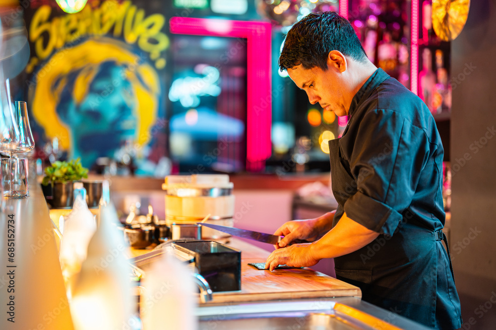 Side view of Chef holding knife and cutting nori seaweed on chopping board at illuminated counter in bar Side view of Chef holding knife and cutting nori seaweed on chopping board at illuminated counter in bar