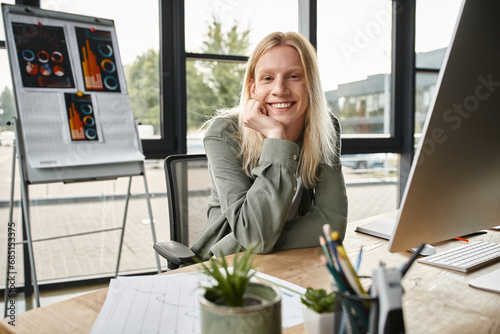 joyful attractive non binary person smiling at camera with hand under chin, business concept photo