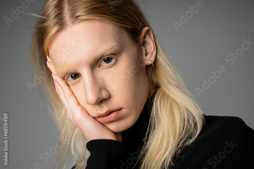 portrait of young non binary person in stylish black turtleneck with hand on face looking at camera