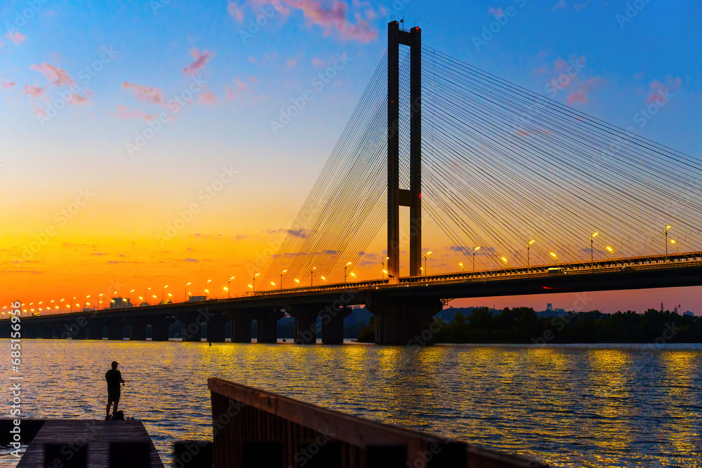 Naklejka premium Sunset Serenity: Cable-Stayed Bridge and Silhouetted Fisher