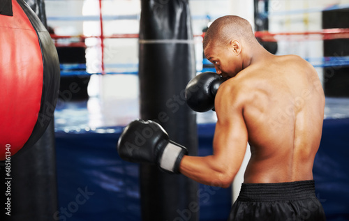 Black man, boxer and punching bag at gym for workout, exercise or self defense practice in fighting sport. African male person with boxing gloves for indoor training or martial arts at health club © Marine Gastineau/peopleimages.com