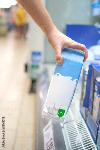 Hand taking a milk carton from supermarket shelf ready for consumption