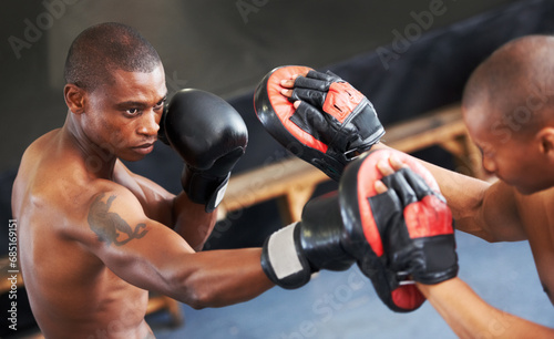Boxing, training and black man with personal trainer for fitness, power or coaching challenge. Strong body, sparring partner and boxer in gym with fist up, workout and confidence in competition fight © Marine Gastineau/peopleimages.com