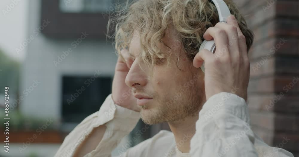 Close-up portrait of relaxed guy putting on headphones listening to music enjoying walk outside in city. Modern lifestyle and youth culture concept. Close-up portrait of relaxed guy putting on headphones listening to music enjoying walk outside in city. Modern lifestyle and youth culture concept.