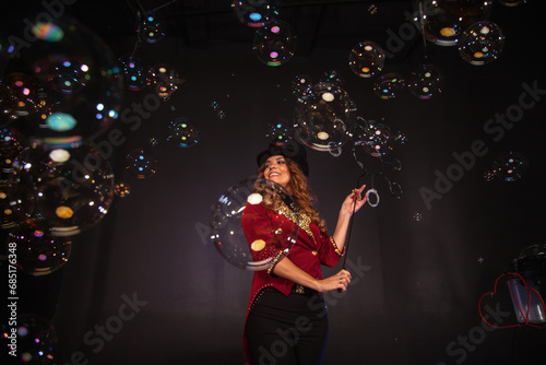 Perfect circus actor lady shows on theatre stage, happy look. Magician illusionist woman in red costume, top hat performing soap bubbles show at shadow. Theatrical perform concept. Copy ad text space