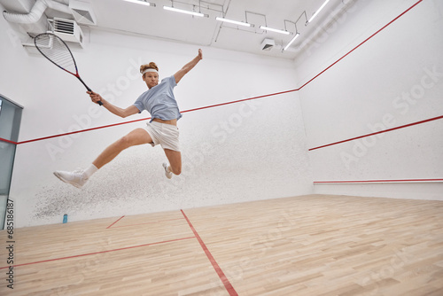 motion shot, active player holding racquet and jumping while playing squash inside of court